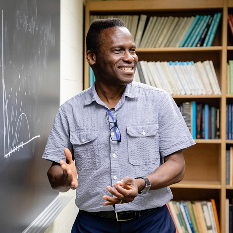 Professor smiling near chalkboard.