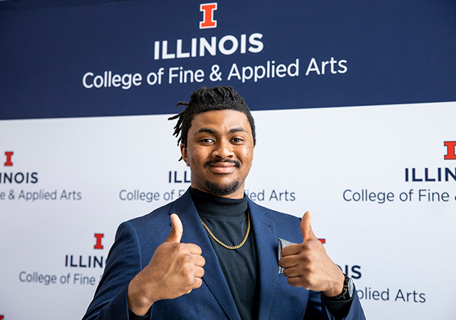 student posing in front of a College of Fine and Applied Arts backdrop