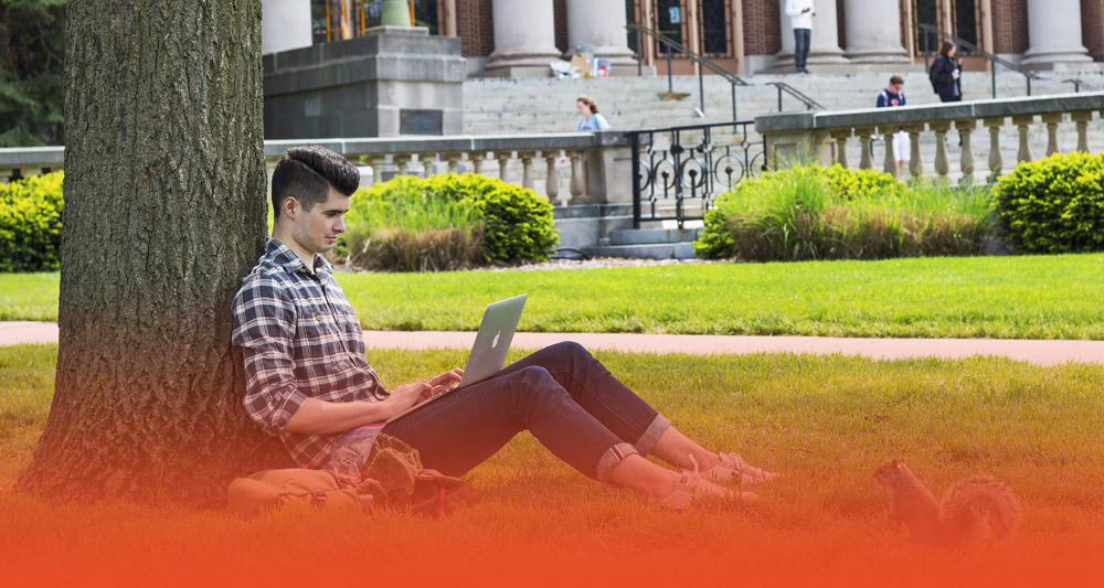 student working on their laptop on the Quad with a little squirrel buddy