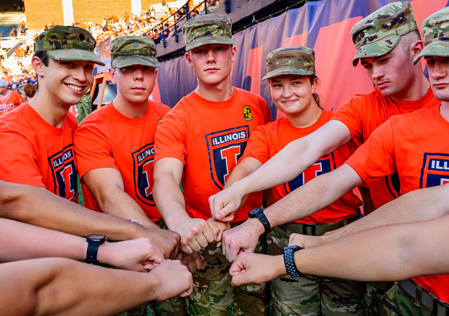 members of ROTC huddle with hands in at Illini football game
