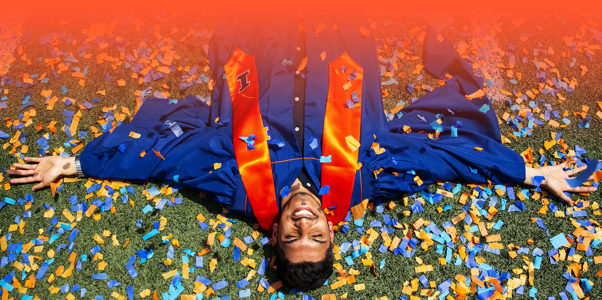recent graduate laying in a pile of confetti celebrating during commencement at Memorial Stadium
