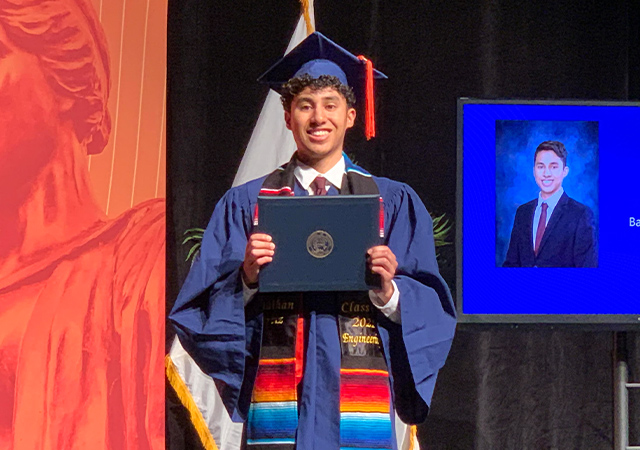 Jonathan holding his diploma dressed in graduation regalia at Commencement