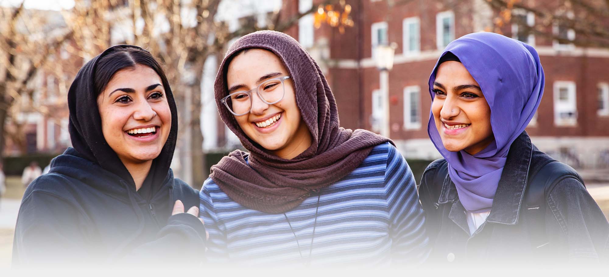 three friends in hijab posing with one another on the Quad