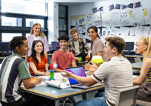 high school students sitting around a table having a discussion with their teacher